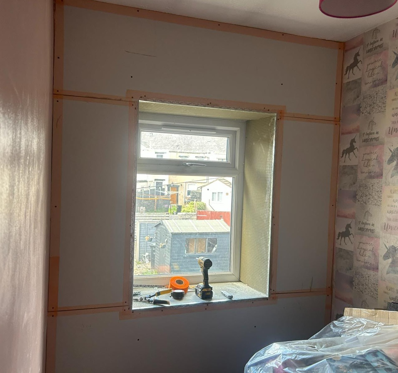 Plasterboard dotted and dabbed around a window, joints taped, drill on the sill