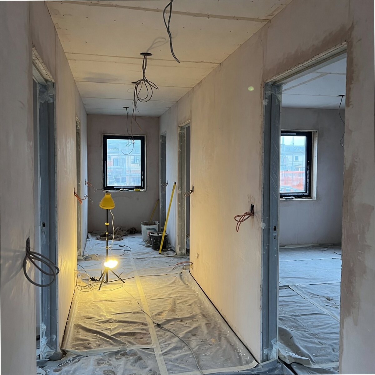 New-build hallway with boarded walls, drop sheets, door liners and hanging cables
